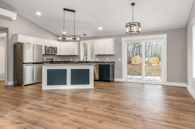 kitchen featuring stainless steel appliances, a wall mounted AC, hanging light fixtures, sink, and white cabinetry