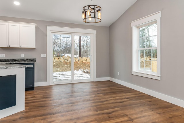 unfurnished dining area featuring lofted ceiling, dark hardwood / wood-style flooring, and an inviting chandelier