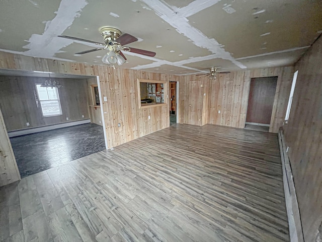 unfurnished living room with baseboard heating, ceiling fan, wood walls, and dark hardwood / wood-style floors