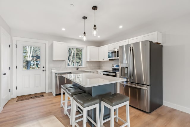 kitchen with hanging light fixtures, light hardwood / wood-style flooring, a kitchen island, white cabinetry, and stainless steel appliances