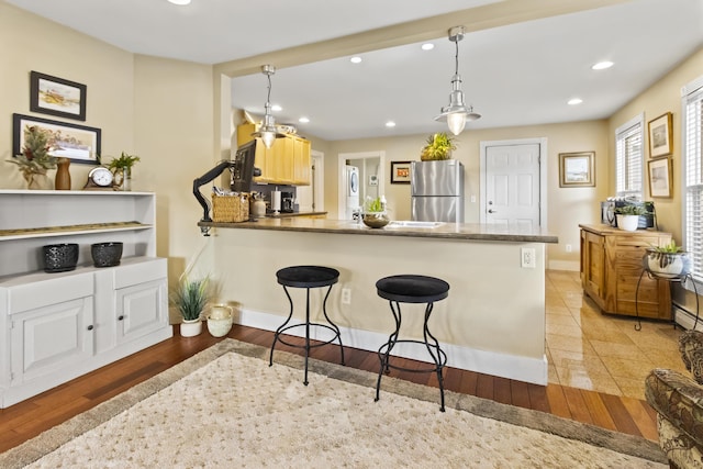 kitchen with light hardwood / wood-style floors, kitchen peninsula, hanging light fixtures, and stainless steel refrigerator