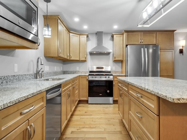 kitchen featuring pendant lighting, wall chimney range hood, sink, light hardwood / wood-style floors, and stainless steel appliances