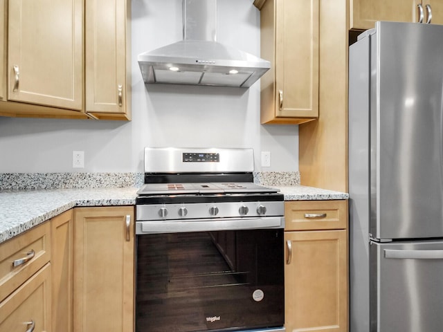 kitchen featuring light brown cabinetry, stainless steel appliances, light stone counters, and wall chimney exhaust hood