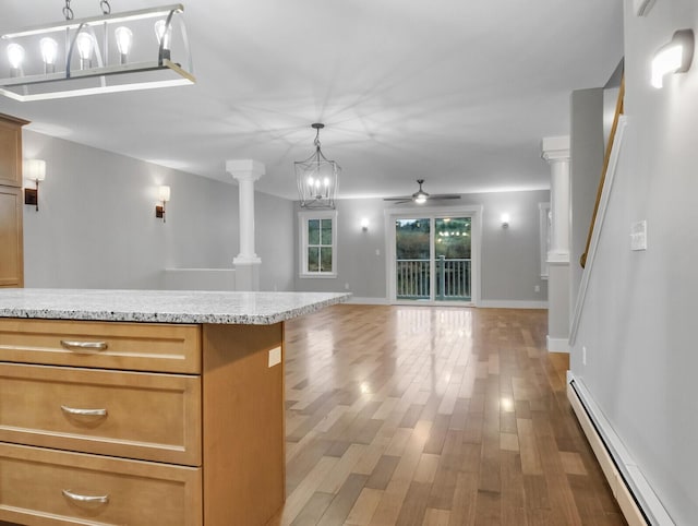 kitchen featuring light stone countertops, ornate columns, ceiling fan with notable chandelier, a baseboard radiator, and hardwood / wood-style flooring