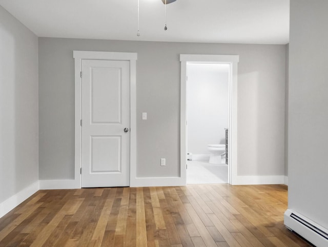 empty room featuring wood-type flooring and a baseboard heating unit