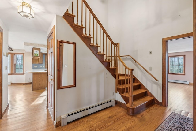 stairway with wood-type flooring, a baseboard radiator, and a wealth of natural light