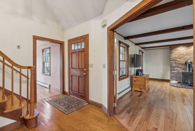 foyer entrance with baseboard heating, a wood stove, and light hardwood / wood-style floors