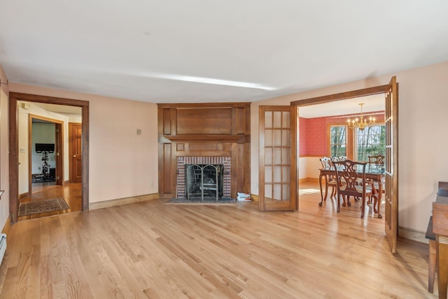 living room featuring french doors, a baseboard radiator, a notable chandelier, a fireplace, and light hardwood / wood-style floors