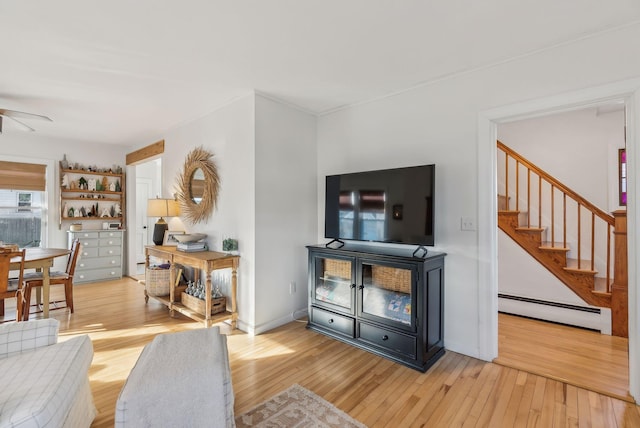 living area with a baseboard heating unit, baseboards, stairway, light wood-type flooring, and a ceiling fan