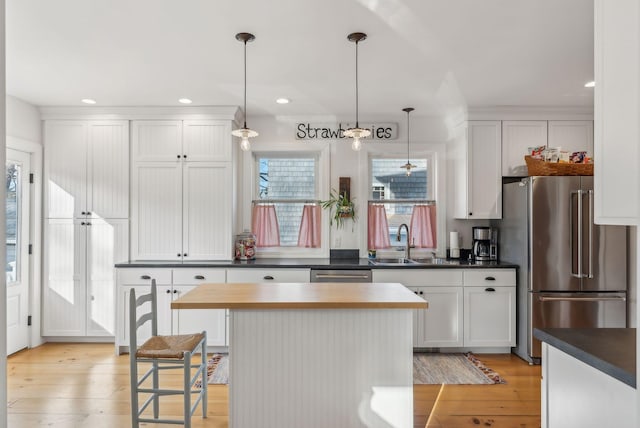 kitchen with dark countertops, a kitchen island, decorative light fixtures, appliances with stainless steel finishes, and light wood-style floors