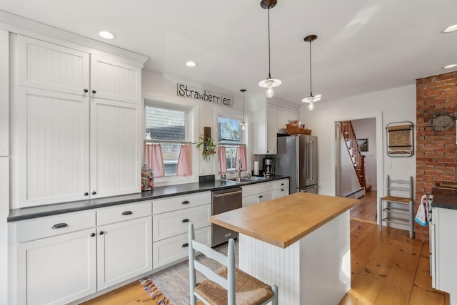 kitchen with light wood-type flooring, butcher block countertops, a sink, appliances with stainless steel finishes, and hanging light fixtures