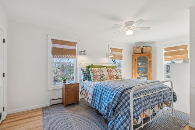 bedroom featuring a ceiling fan, baseboards, light wood-type flooring, and a baseboard radiator