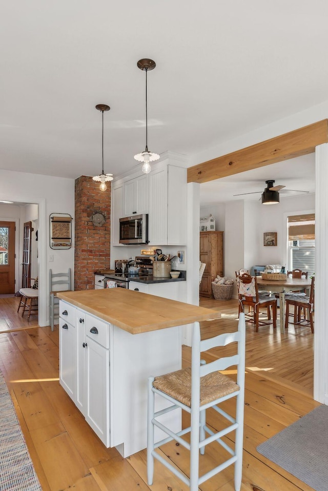 kitchen with white cabinetry, stainless steel appliances, light wood finished floors, wooden counters, and hanging light fixtures