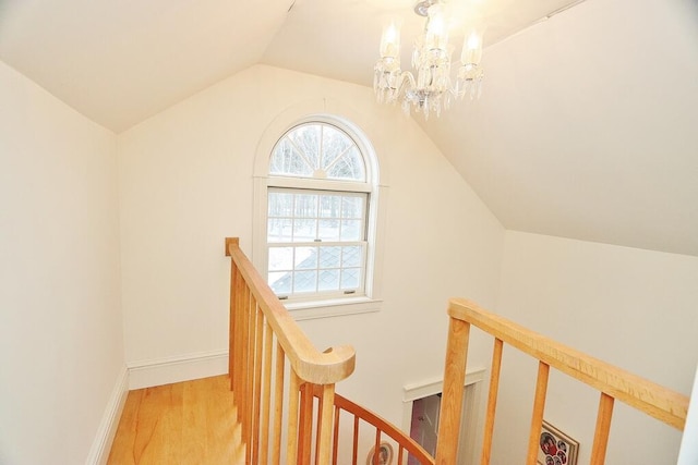 hallway with light hardwood / wood-style flooring, an inviting chandelier, and lofted ceiling