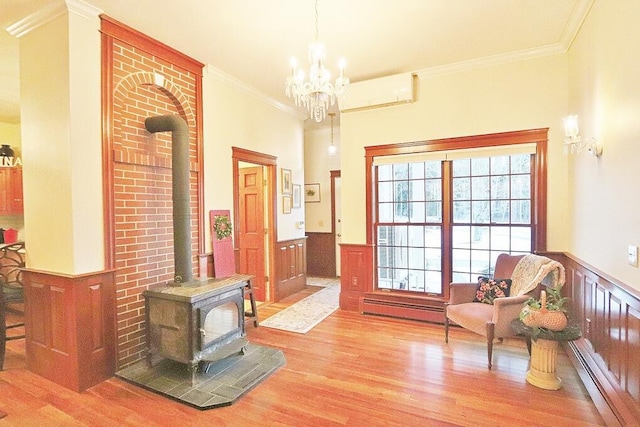 sitting room featuring a wood stove, crown molding, a baseboard radiator, a wall unit AC, and a chandelier