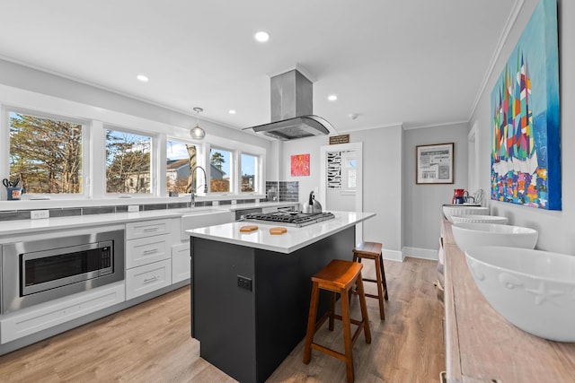 kitchen featuring appliances with stainless steel finishes, ornamental molding, island range hood, a center island, and white cabinetry