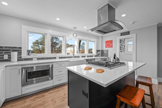 kitchen featuring stainless steel appliances, island range hood, sink, a kitchen island, and a breakfast bar area