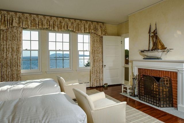 bedroom with a water view, dark hardwood / wood-style floors, and a brick fireplace