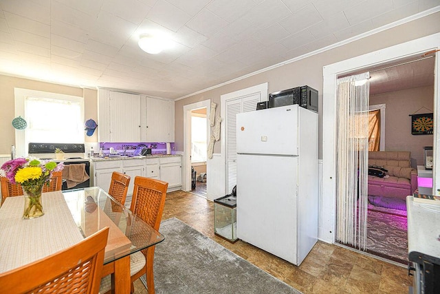 kitchen featuring crown molding, plenty of natural light, white cabinets, and white appliances