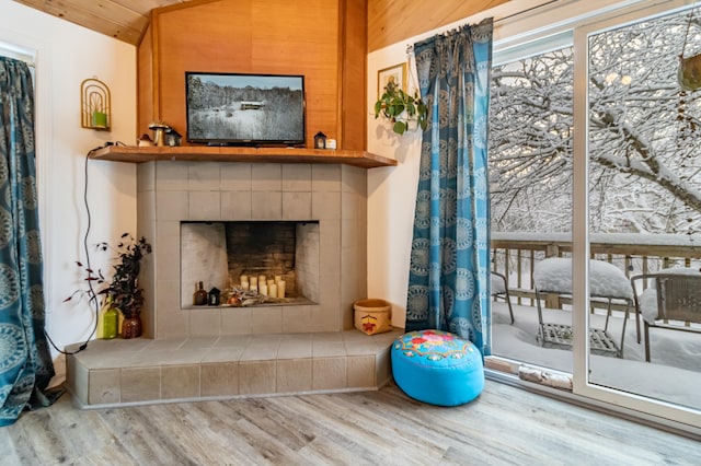 interior space with wooden ceiling, vaulted ceiling, wooden walls, a fireplace, and light wood-type flooring