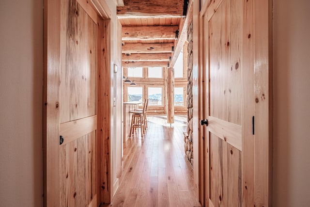 hallway with beamed ceiling, light hardwood / wood-style floors, wood ceiling, and rustic walls