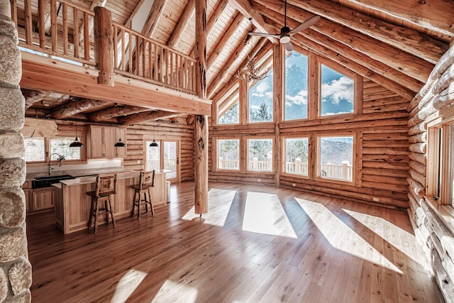 unfurnished living room featuring log walls, light hardwood / wood-style flooring, high vaulted ceiling, and beamed ceiling