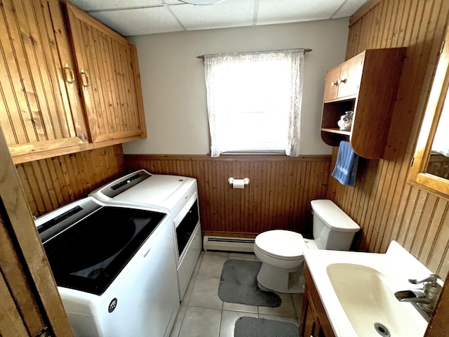 clothes washing area with wood walls, a baseboard heating unit, sink, washer and dryer, and light tile patterned floors