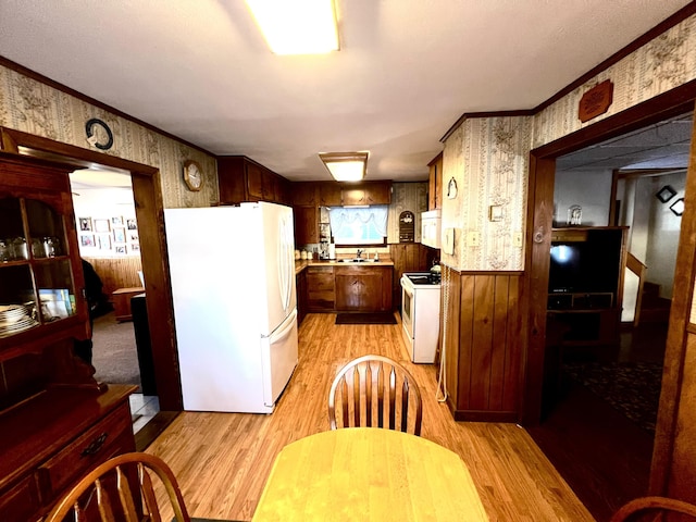 kitchen with white appliances, crown molding, sink, wooden walls, and light wood-type flooring