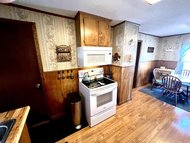 kitchen with wood walls, light hardwood / wood-style floors, white appliances, and crown molding