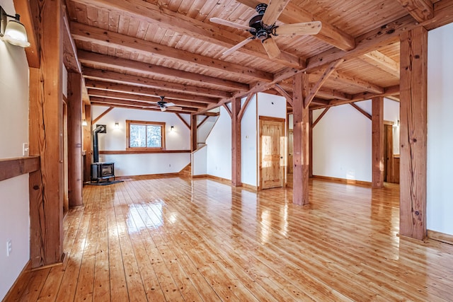 unfurnished living room with beam ceiling, a wood stove, ceiling fan, wooden ceiling, and light wood-type flooring