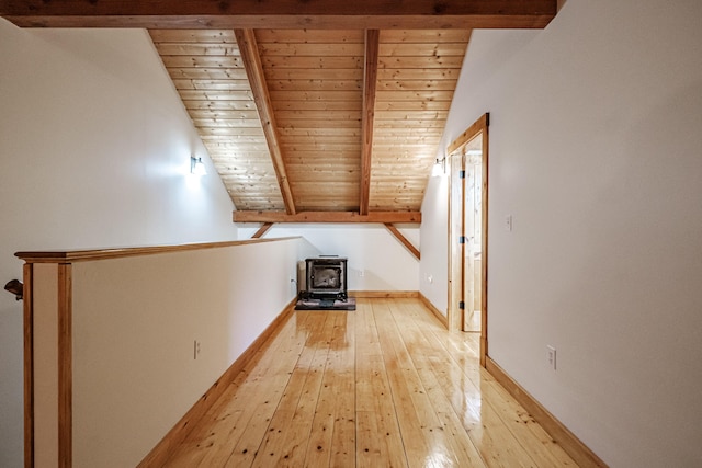 additional living space with a wood stove, light hardwood / wood-style flooring, wood ceiling, and vaulted ceiling with beams