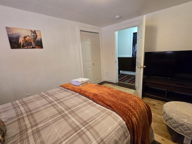 bedroom with a closet, a baseboard heating unit, and light hardwood / wood-style flooring