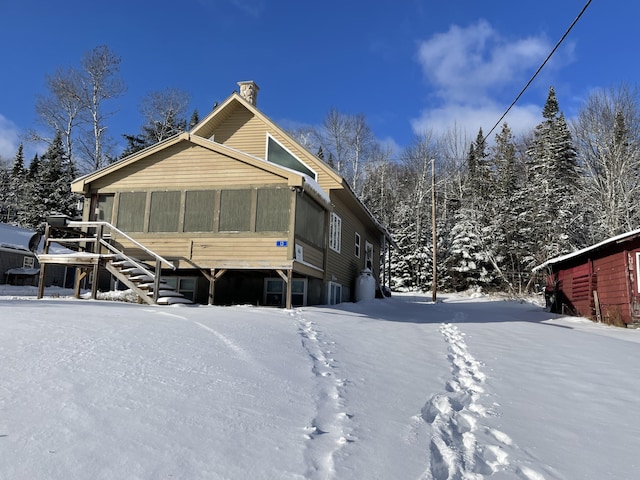 snow covered back of property featuring a sunroom