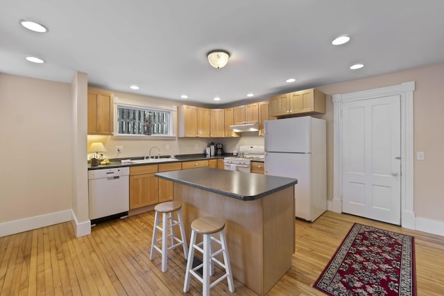 kitchen with a breakfast bar, white appliances, light hardwood / wood-style floors, and a kitchen island