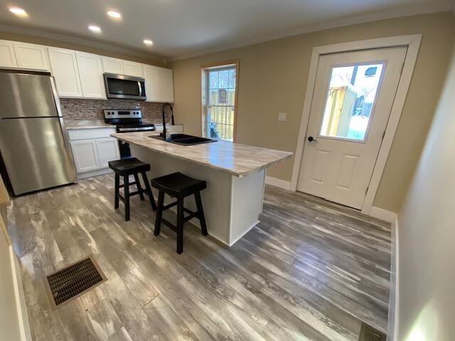 kitchen featuring visible vents, ornamental molding, wood finished floors, stainless steel appliances, and a sink