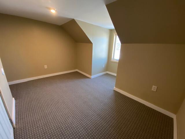 bonus room featuring vaulted ceiling, dark colored carpet, and baseboards