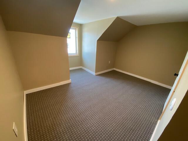 bonus room with lofted ceiling, dark carpet, and baseboards