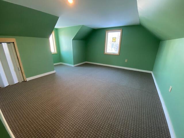 bonus room with lofted ceiling, baseboards, and dark colored carpet