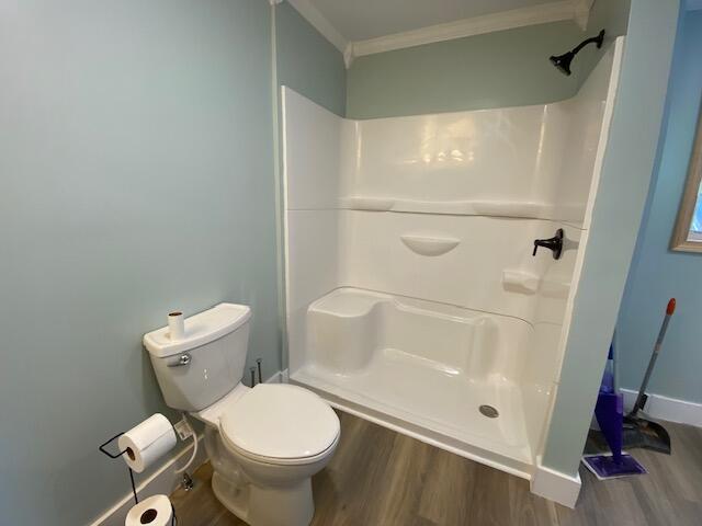 bathroom with toilet, wood finished floors, baseboards, ornamental molding, and a stall shower