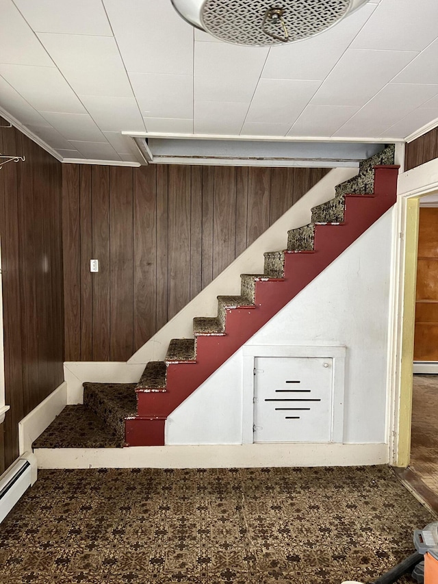 staircase with wooden walls and a baseboard heating unit