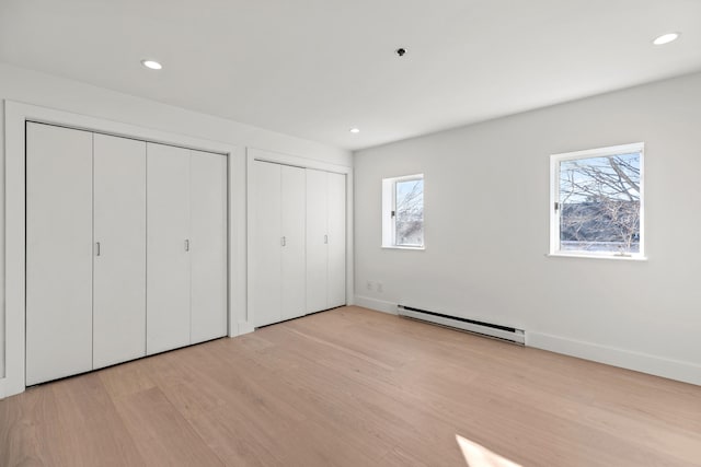 unfurnished bedroom with multiple closets, light wood-type flooring, multiple windows, and a baseboard heating unit