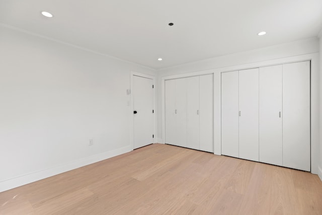 unfurnished bedroom featuring light wood-type flooring and multiple closets