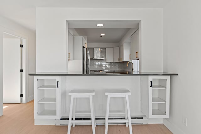 kitchen featuring kitchen peninsula, light wood-type flooring, baseboard heating, and backsplash