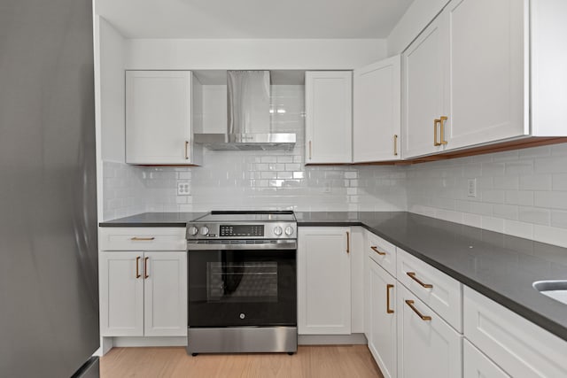 kitchen with white cabinets, appliances with stainless steel finishes, light wood-type flooring, and wall chimney range hood