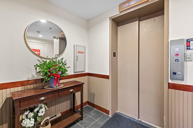 hall featuring elevator, dark tile patterned flooring, and wood walls