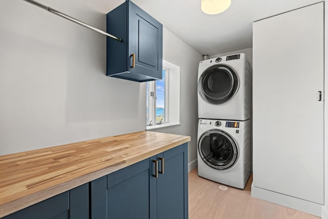 laundry room with cabinets, stacked washing maching and dryer, and light wood-type flooring