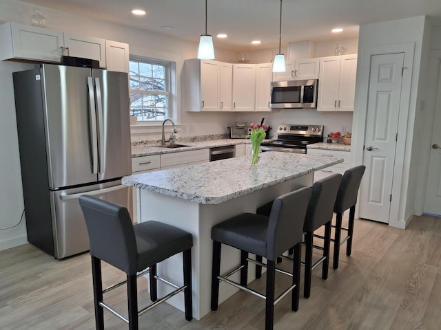 kitchen featuring appliances with stainless steel finishes, a kitchen island, sink, white cabinetry, and hanging light fixtures