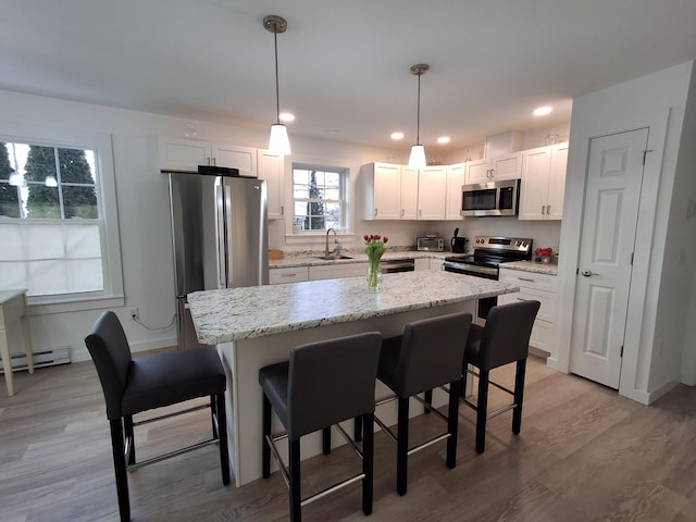 kitchen with sink, light hardwood / wood-style flooring, appliances with stainless steel finishes, decorative light fixtures, and white cabinetry