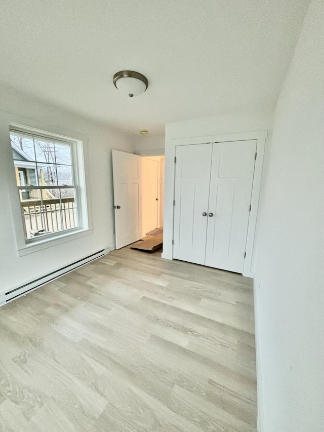 unfurnished bedroom featuring a closet, baseboard heating, and light hardwood / wood-style floors