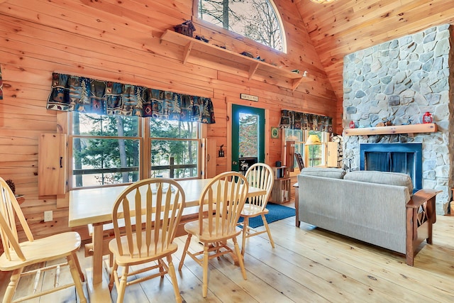 dining space featuring high vaulted ceiling, wood walls, light hardwood / wood-style floors, a fireplace, and wood ceiling